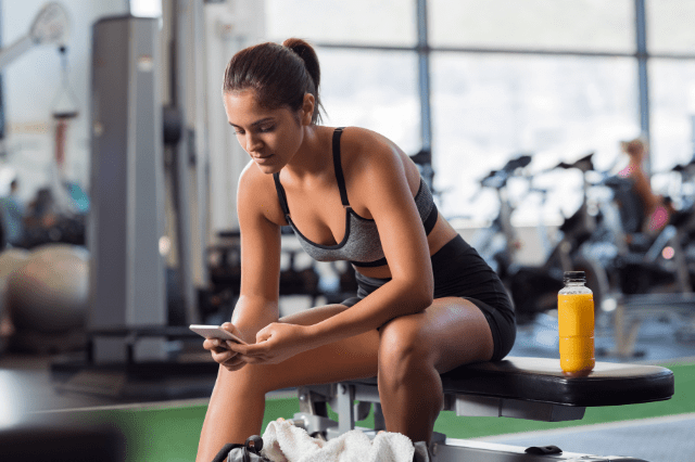 Young girl in the gym, having a short break in between a workout session. She is checking her personalised fitness plan.