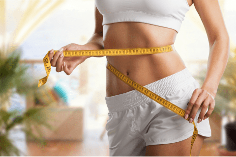 A woman measuring her waist after successfully completing a fat loss program, demonstrating her progress and achievement in her fitness journey.