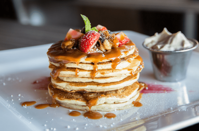 Golden pancakes topped with a vibrant assortment of fresh fruits and drizzled with delicious syrup, creating a tempting and mouth-watering breakfast or brunch spread.